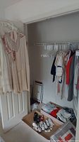 Closet with various vintage dresses hanging, shoes on floor including white tap shoes, jackets and jumpers visible