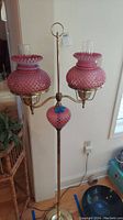 Full view of brass floor lamp with two cranberry hobnail glass shades and central accent