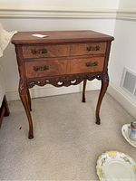 Front angle photo showing the carved legs, two drawers with decorative brass handles, and carved detailing on the apron.