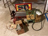 Photo showing all items in group: metal Erector set, green toy oven, Jack-in-the-Box clown, and tin man toy on a concrete floor.