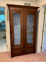 Front view showing full height vintage wood cabinet with glass doors, glass shelves inside, and drawers below.