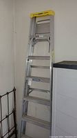 Full view of Werner aluminum step ladder, 8 feet tall, leaning against wall indoors.
