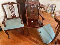 Two matching carved wooden armchairs with custom light blue cushions on hardwood floor. One cushion is removed and placed nearby.