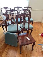 Group of six carved wood chairs with light blue cushions arranged around a dining table on hardwood flooring.