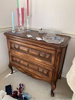 Front and side angle showing full wood chest with two drawers adorned with metal handles, decorative carvings, and curved legs.