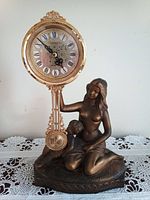 Front view of Citizen mantel clock featuring bronze-colored figurine of a woman and child, ornate clock face with Roman numerals and swinging pendulum.
