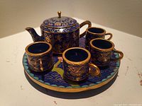Full view of the miniature cloisonne tea set displayed on the tray, showing teapot and four cups with blue and gold floral patterns.