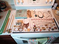 Full layout of all costume jewellery items on towel on stove top, showing necklaces, bracelets, earrings and brooches.