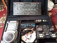 Overall shot of DJ equipment including DJ controller, mixer with cables, CD player and amplifier in a black carrying case on carpeted floor