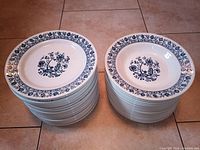 Stack of white 9-inch dinner plates with blue floral and bird design and detailed blue border pattern, arranged on floor.