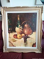 Framed oil on canvas still life painting displayed on couch, showing the full artwork and ornate gold frame.