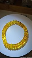 Photo of the chunky golden amber juicy translucent bracelet on a white surface under natural/ambient light to show color and bead shape.