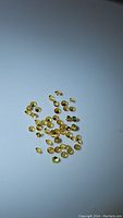 Photo of multiple small round faceted golden yellow sapphire gemstones scattered on white background.