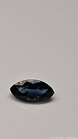Photo of marquis cut blue sapphire gemstone laying flat, showing facets and color.