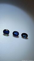 Three oval cut deep blue sapphire gemstones under spotlight showing color and clarity.