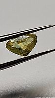 Pear-shaped yellow greenish blue sapphire held by tweezers, showing faceted mixed cut look and natural color nuances.