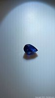 Deep blue pear cut sapphire, 0.80 carat, 7x5mm size shown against a neutral background with light highlighting facets and color.