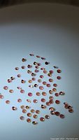 Multiple small round sapphire gemstones with pink-orange padparadscha coloration, arranged on a white background.