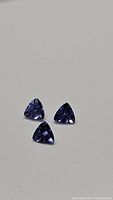 Three natural trillion cut tanzanite gemstones on a gray background, showing shape, color and luster.