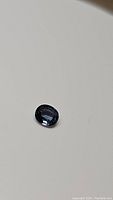 Close-up photo of a single oval cut blue spinel gemstone on a plain surface, showing its size and color.