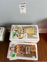 Two Avon Presidents Club dolls arranged in molded white styrofoam packaging, one dressed in mustard yellow and the other in light yellow with sunflower accents.