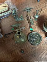 Brass tea pot, candleholder, figurines, letter opener, and various small brass decor items laid out on a wooden floor.