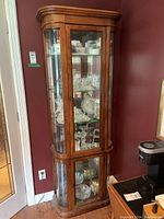 Tall wooden vintage display cabinet with glass panels and five glass shelves, filled with glassware and collectibles.