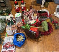 Overall lot contents on floor showing assortment of Christmas decorations including nutcrackers, wreath, skating pond, sleigh, ribbons, lantern, and other decorative items