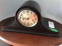 Front view of wooden quartz mantle clock, showing clock face and curved wooden casing.