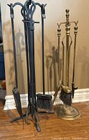 Photo showing two sets of fireplace tools, one brass and one black metal, each with a stand including brush, poker, and shovel.