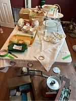 The folding table covered with assorted dinnerware and baskets, viewed from a corner angle showing table top and partial legs.