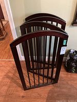 Four identical wooden sections of a foldable gate, with dark wood finish and vertical metal bars folded together.