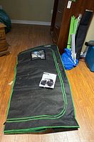 Folded black Vivosun grow tent with green trim, instruction manual placed on top, tent fabric visible on floor.