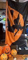 Front view showing the Halloween flag hanging with three orange pumpkins below, one large with light-up cord, one medium and one small.