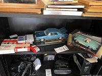 Two model cars, playing cards, quiz booklets, and dominoes on a shelf
