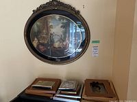 Full view showing the oval framed print hanging on a wall with two smaller framed paintings stacked beneath it.