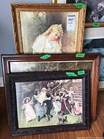 Three framed prints stacked together: a girl portrait in an ornate gold frame, and two prints of scenes with children and possibly a hunt in wood frames.