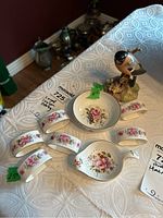 Overview of all porcelain items including the bird figurine, small bowl, tea strainer, and five napkin rings arranged on a table.