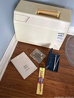 Closed sewing machine with carrying case, instruction manual, and sewing notions on floor.