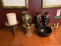 Full view of lot including brass vase, ceramic vases, metal candle holder with white candle, brass angel figurine, black bowl, and brass armillary sculpture on wooden table.