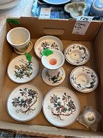 Top-down view of all ceramic items in a box showing floral designs on plates and ramekins along with candleholders and small pot.