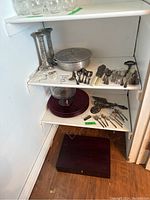 Photo showing two silverplate candlesticks, vintage aluminum lidded casserole dish with Pyrex dish, and various flatware on shelves.