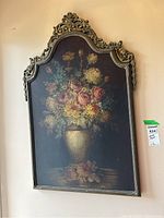 Front view of metal wall art showing floral vase painting and ornate frame against wall.