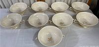 Set of ten white Lenox soup cups with gold wave design arranged on table.