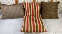 Shows three pillows: one rectangular brown striped, two square pillows (one brown textured, two striped red, yellow, and brown)