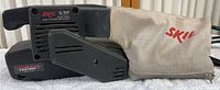 Side view of Skil 3/4 HP 3-Inch Belt Sander with dust collection bag attached. The bag is beige and branded with red 'SKIL' lettering.