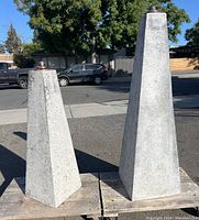 Photo showing both hollow concrete tiki torch statues outdoors on wooden pallets with street background.