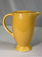 Full view of yellow ceramic Fiesta Ware pitcher standing upright showing handle and spout