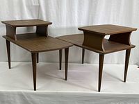 Two matching mid century side tables with faux walnut Formica tops and raised lamp risers, four tapered unscrewing legs each.