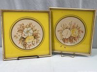 Two square wood framed vintage floral prints with yellow circular painted mats on glass, displayed standing on a flat surface.